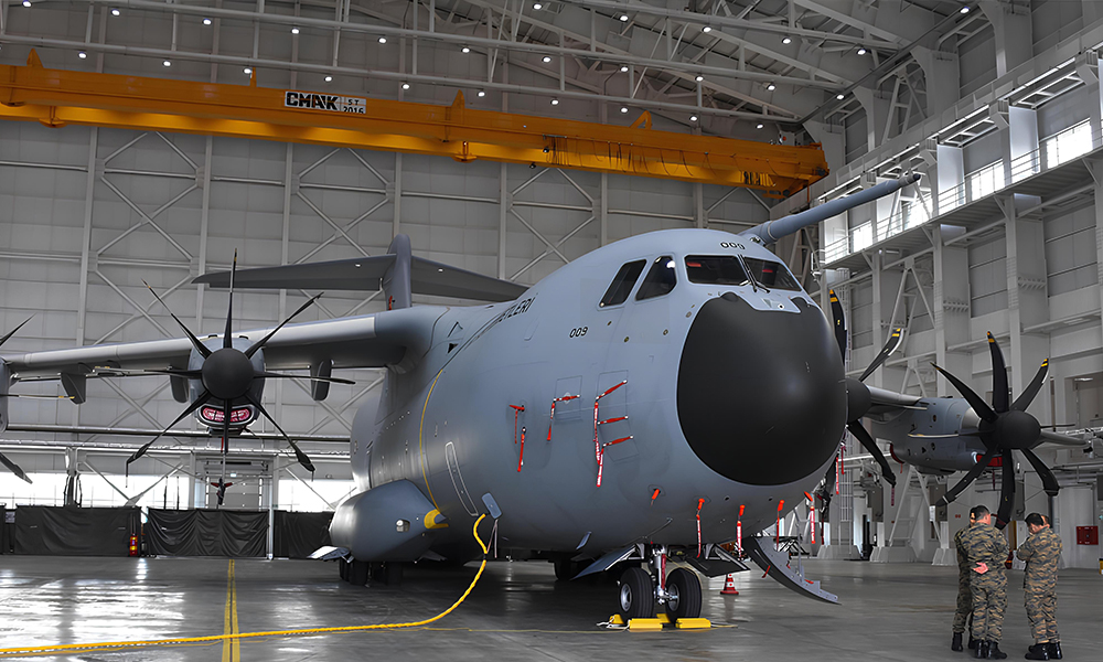 A heavy-duty double-girder bridge crane manufactured by CMAK Crane Company installed inside a military aircraft hangar bay next to a large military transport plane.