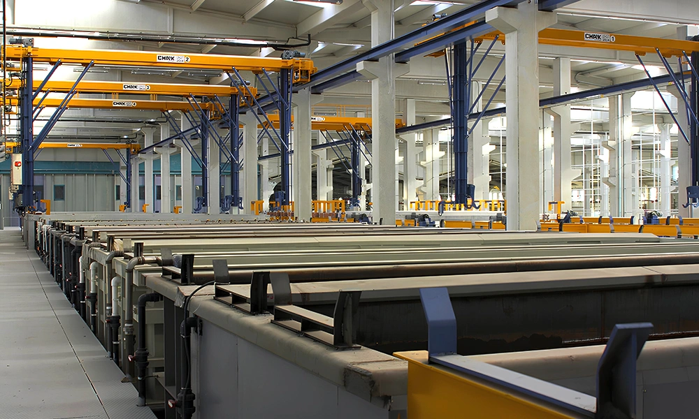 Multiple automated yellow overhead dipping machines from the special cranes CMAK lineup, configured with heavy-duty vertical stabilization arms operating seamlessly across a long row of industrial chemical treatment tanks.