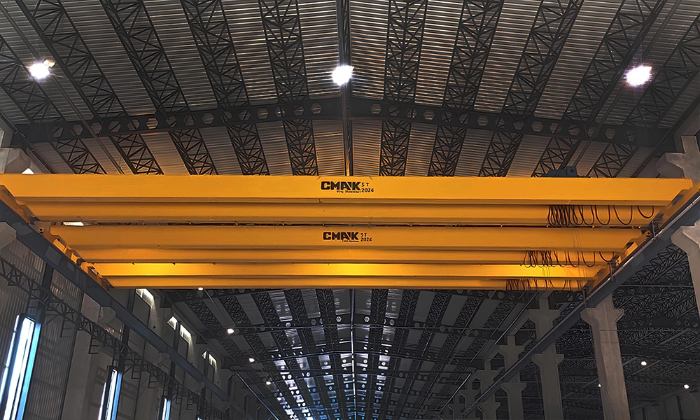 Yellow 5-ton capacity CMAK double-girder bridge cranes operating inside a long, high-ceiling industrial warehouse facility.