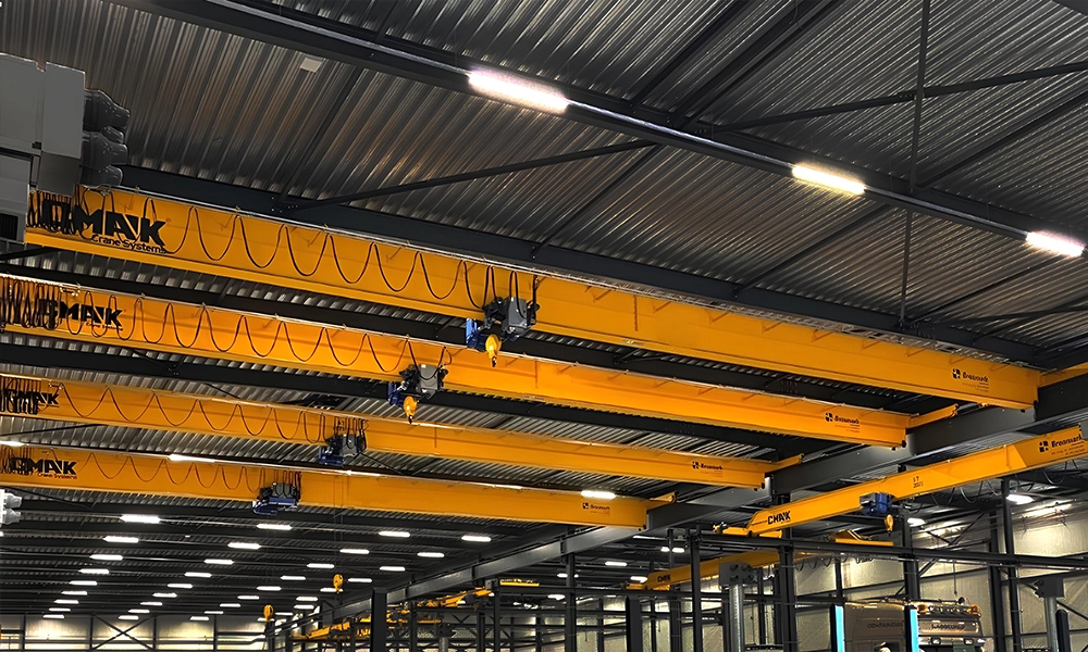 Close-up view of multiple yellow CMAK single-girder bridge cranes featuring wire rope hoists and clean festoon cable tracking systems underneath a corrugated warehouse roof.