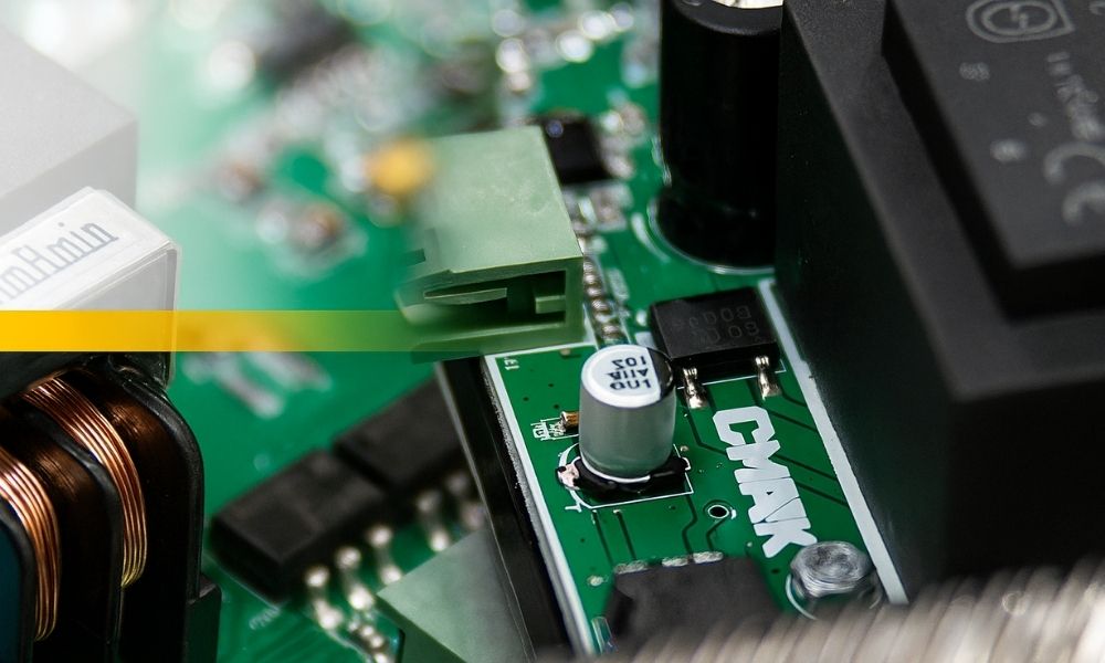 Close-up view of the printed circuit board (PCB) hardware with integrated microchips and capacitors for the HoistSense Crane Monitoring system, showcasing the branded CMAK electronic architecture.