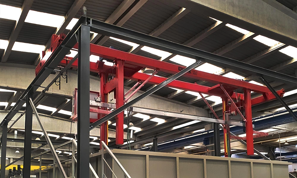 A custom red dipping process machine engineered from the special cranes CMAK series, featuring a rigid vertical lifter and stabilizer frame operating over industrial chemical processing tanks.