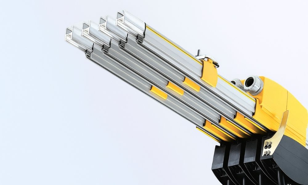 Close-up view of a four-pole copper conductor bar assembly showing the aluminum profiles, protective yellow clips, and the terminal power feed connection block of PVC enclosed busbar systems.