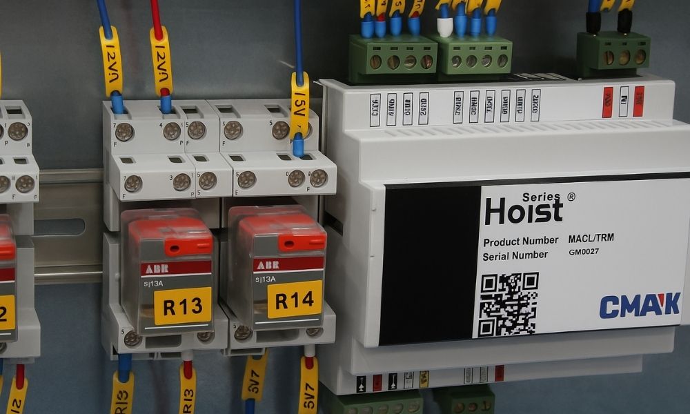 Inside an electrical panel showcasing the HoistSense Crane Monitoring hardware module labeled "Hoist Series", installed alongside ABR industrial relays and labeled wiring terminals.